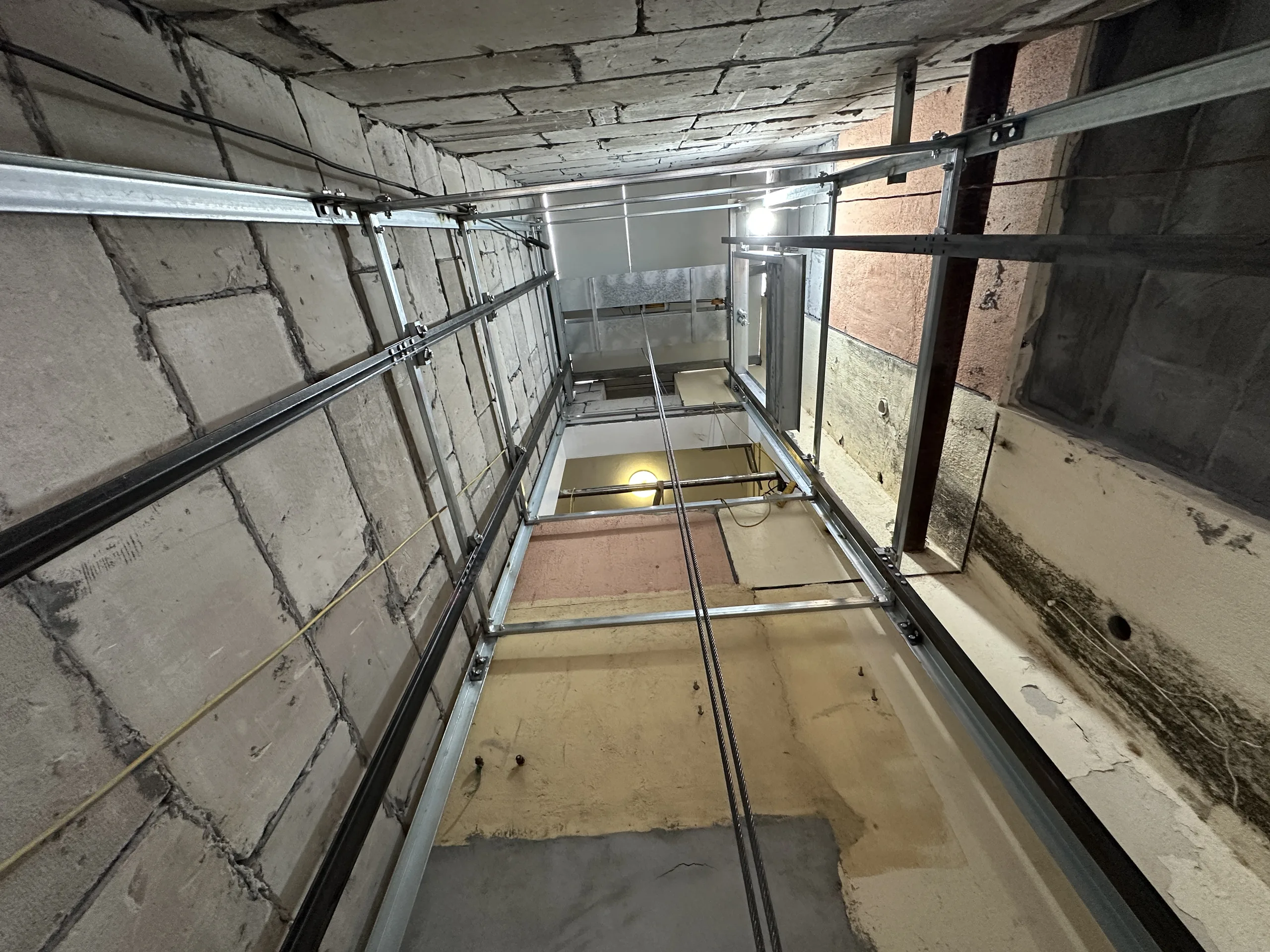 Dumbwaiter inspection of a metal shaft showing guide rails, landing doors and pit condition